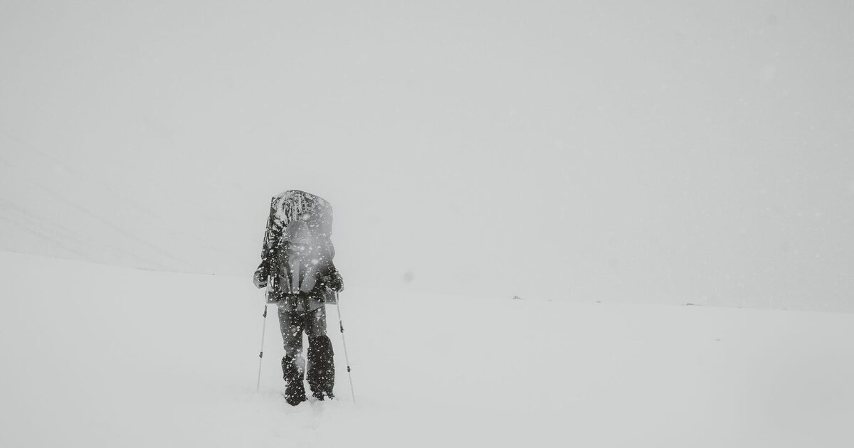A lone figure walking through a whiteout, almost erased by the snow