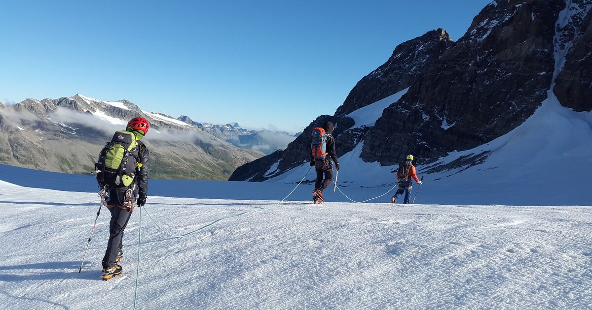 Roped climbers crossing a snowfield together toward a mountain ridge