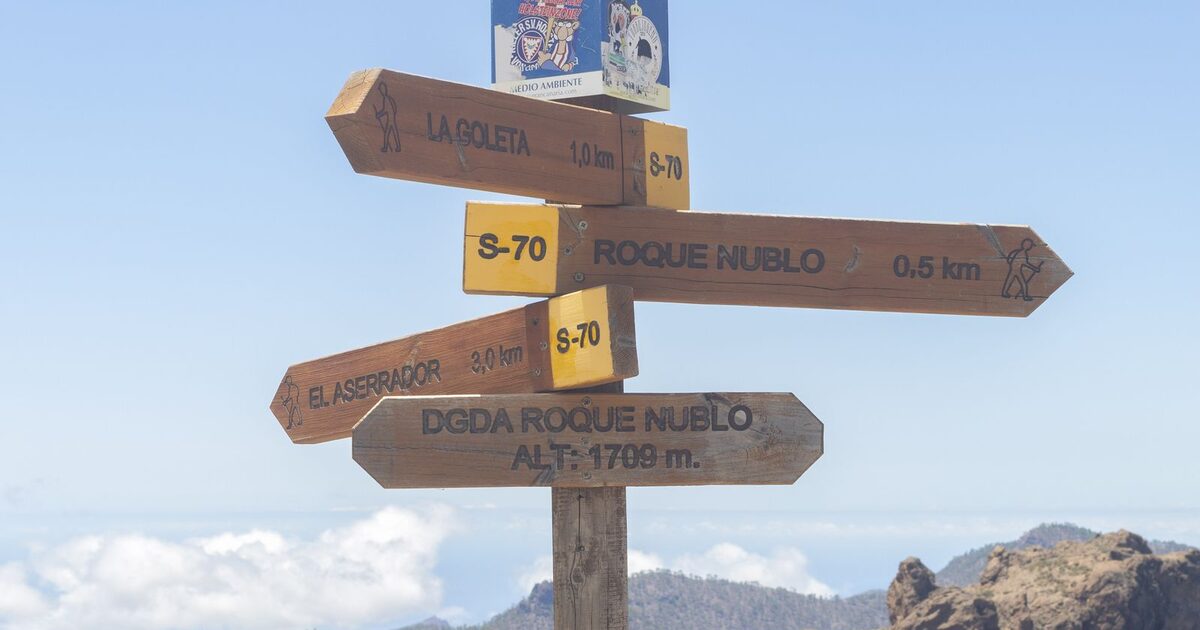 A wooden trail signpost pointing in two directions on a mountain ridge, standing in for the AI comparison decision a shopper never sees resolved on a brand's own page