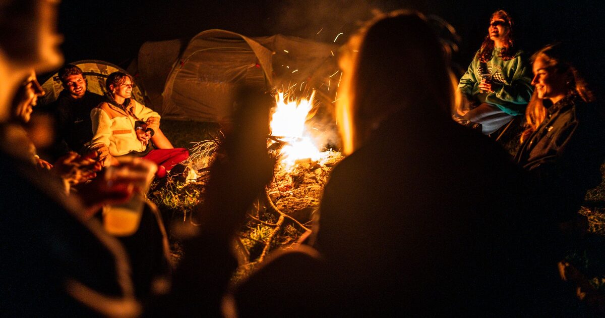 People gathered close around a campfire at night, talking in the firelight