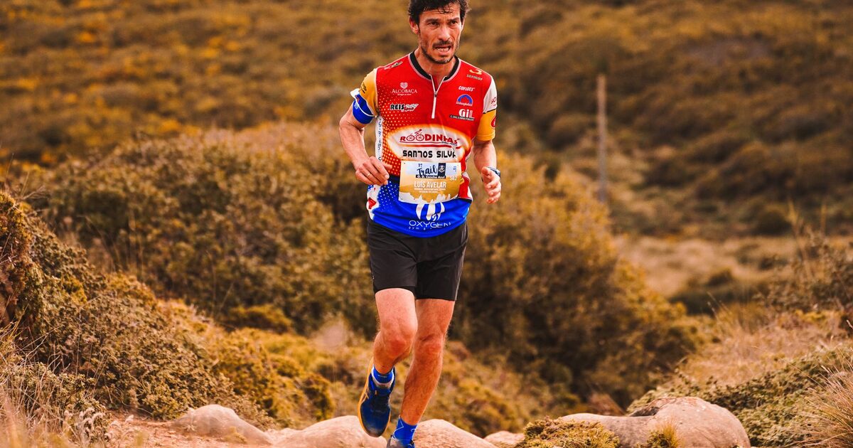 A trail runner mid-stride on a hillside path, moving fast through open country