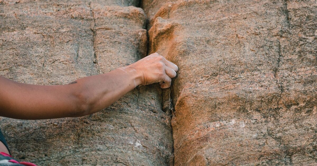 A climber's hand gripping a crack in a granite wall, pulling up to the next hold