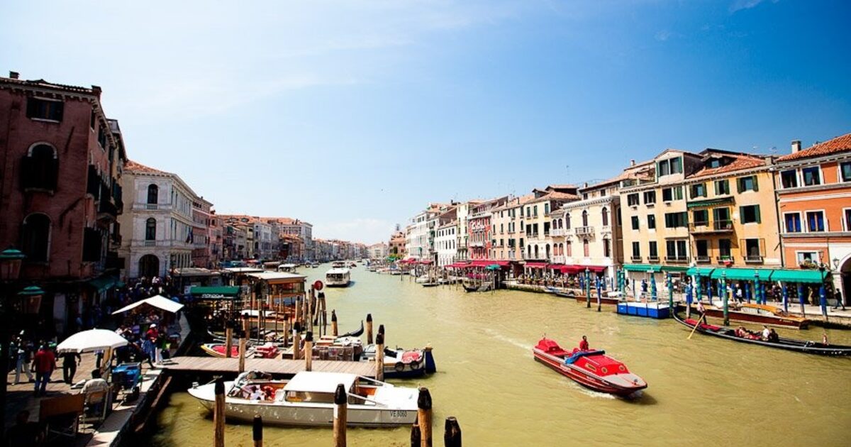 A busy canal in Venice full of boat traffic, most passing straight through without stopping at any dock