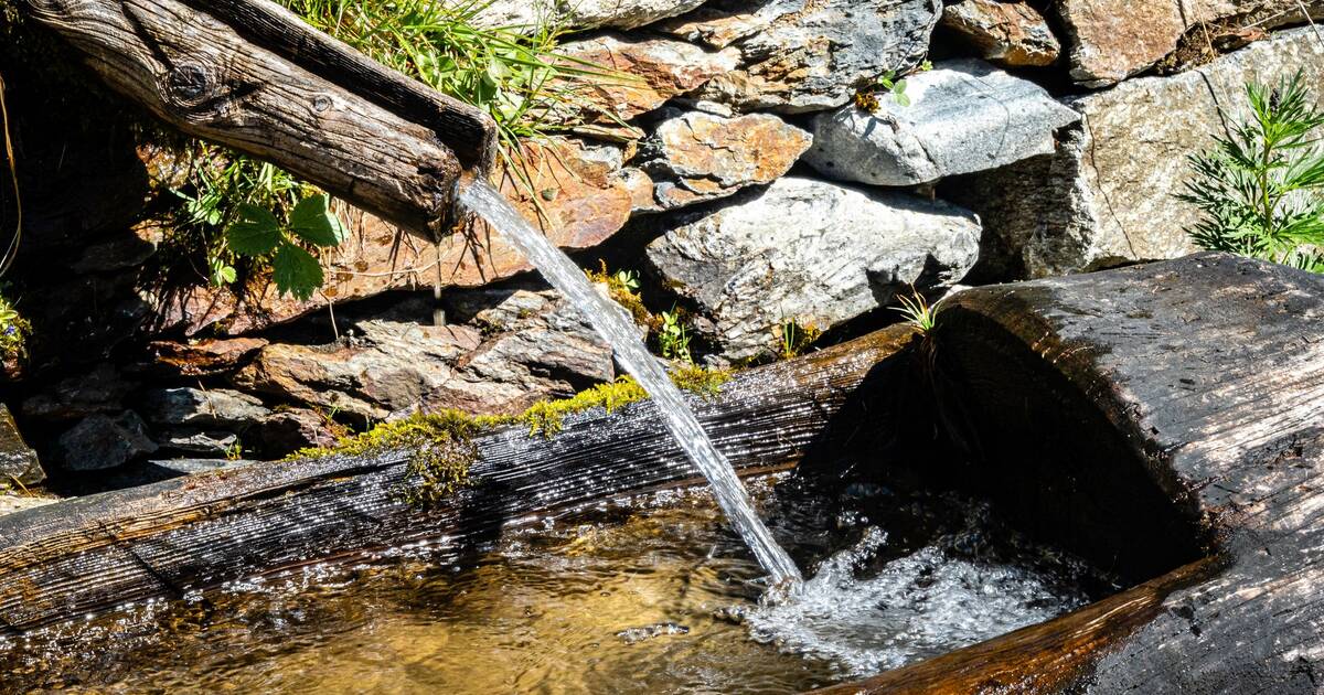 Clear spring water running from a stone spout into a rocky mountain basin
